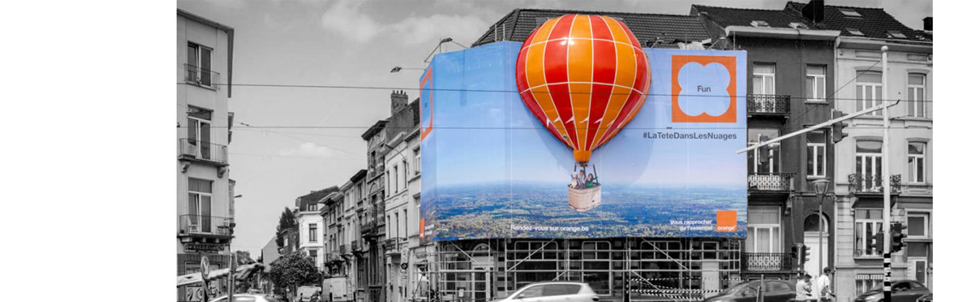 Large inflatable promotional material | X-Treme Creations combination of inflatable balloon shape Orange with a large 2D frontlit banner against the façade of a building commissioned by the agency Pop-Media Orange Pop-Media X-Treme Creations