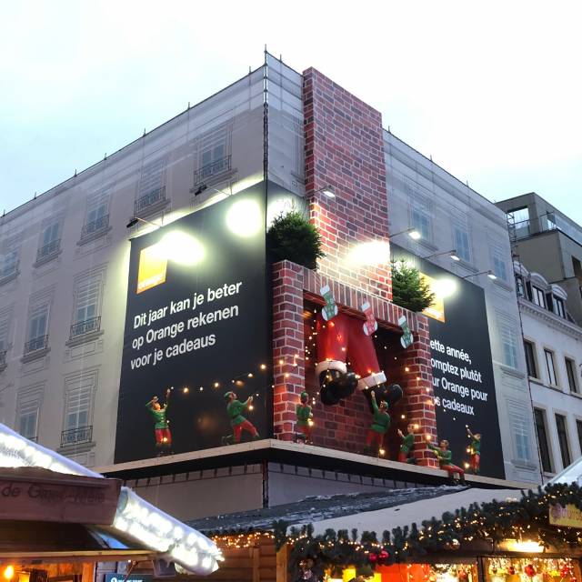 Combineer print en opblaasbaar opblaasbare benen van een inflatable kerstman tegen een façade als Kerstmis decoratie te Brussel voor klant Pop media met permanente blower X-Treme Creations