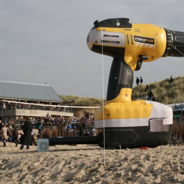 Riesige aufblasbare Produktvergrößerungen Aufblasbare Bohrmaschine Powerplus mit Akku als 4 m hohe Produktvergrößerung am Strand X-Treme Creations