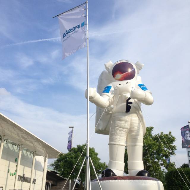 Mascottes et personnages gonflables géants Astronaute gonflable sur base tenant un drapeau Fespa à louer à l'entrée principale de l'Exposition Mondiale d'Impression digitale et sérigraphie à Cologne X-Treme Creations