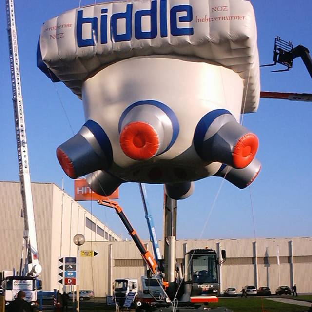 Giant inflatable productuitvergroting opblaasbaar verwarmingssysteem Biddle hangt onder een kraan buiten Flanders' Expo Gent X-Treme Creations